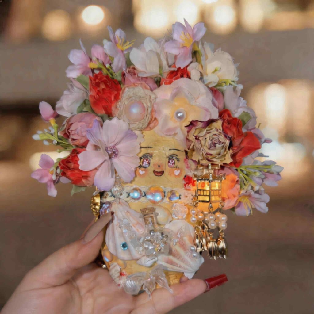 Handmade floral pod doll with pink, red, and ivory blossoms, pearl details, and lantern charm held in hand