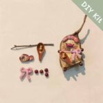 DIY kit materials for Handmade Whimsical Piglet Bell Decor arranged beside the finished design on a neutral background