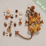 DIY kit materials for Bat-Wing Pod Doll Woodland Cat Bard arranged beside the finished design on a neutral background