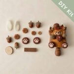 DIY kit materials for Swing-Tail Cat Pod Doll Autumn Acorn Kitty arranged beside the finished design on a neutral background