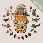 Flat lay of a handmade ornate pod doll surrounded by red-and-blue floral ornaments, bird motifs, and jewelry-inspired decorative pieces