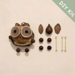 Flat lay of a DIY kit for a handmade pod owl ornament with woodslice eyes, beads, leaf details, and metal connectors
