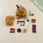 Fuzzy Glasses Monster Pod Doll DIY Kit flat lay with glasses, colorful fabric pieces, mini accessories, and fluffy material components