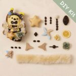 Open-mouth pod doll DIY kit flat lay with star piece, floral parts, fluffy trim, beads, and handmade components