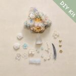 Floral pod doll DIY kit flat lay with white flowers, pearls, lace trim, feather, and pastel decorative parts