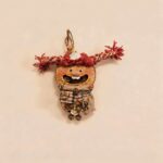 Open-Mouth Pod Doll Scarlet Twiglet with scarlet yarn pigtails, joyful wide smile, and rustic layered handmade details on a neutral background