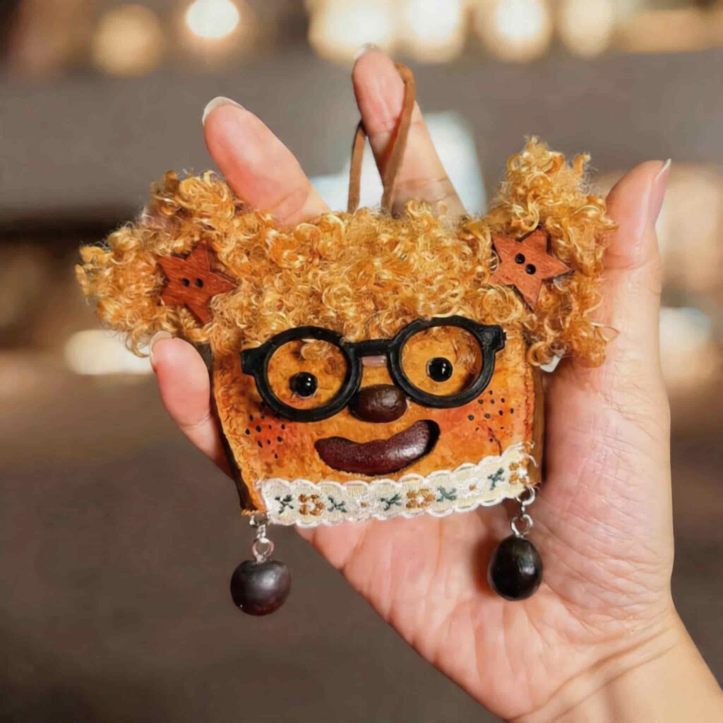 Handheld close-up of a handmade toast-inspired pod doll with curly hair, round glasses, freckles, and star-shaped hair clips