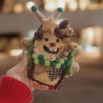 Front view of a handmade open-mouth reindeer pod doll with antler details and coffee bean trim