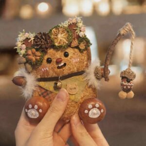 Close-up of a handmade woodland fishing pod doll showing its soft expression, botanical crown, and hanging acorn charm