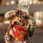 Front view of an open-mouth pod doll featuring a bright red fortune pouch, botanical crown, and cheerful handcrafted face