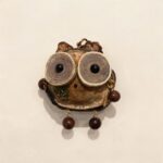Front view of a handmade owl ornament made from a natural pod shell with oversized circular wood eyes