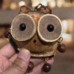 Close-up of a handmade pod owl charm with woodslice eyes, leaf accents, and dangling bead details