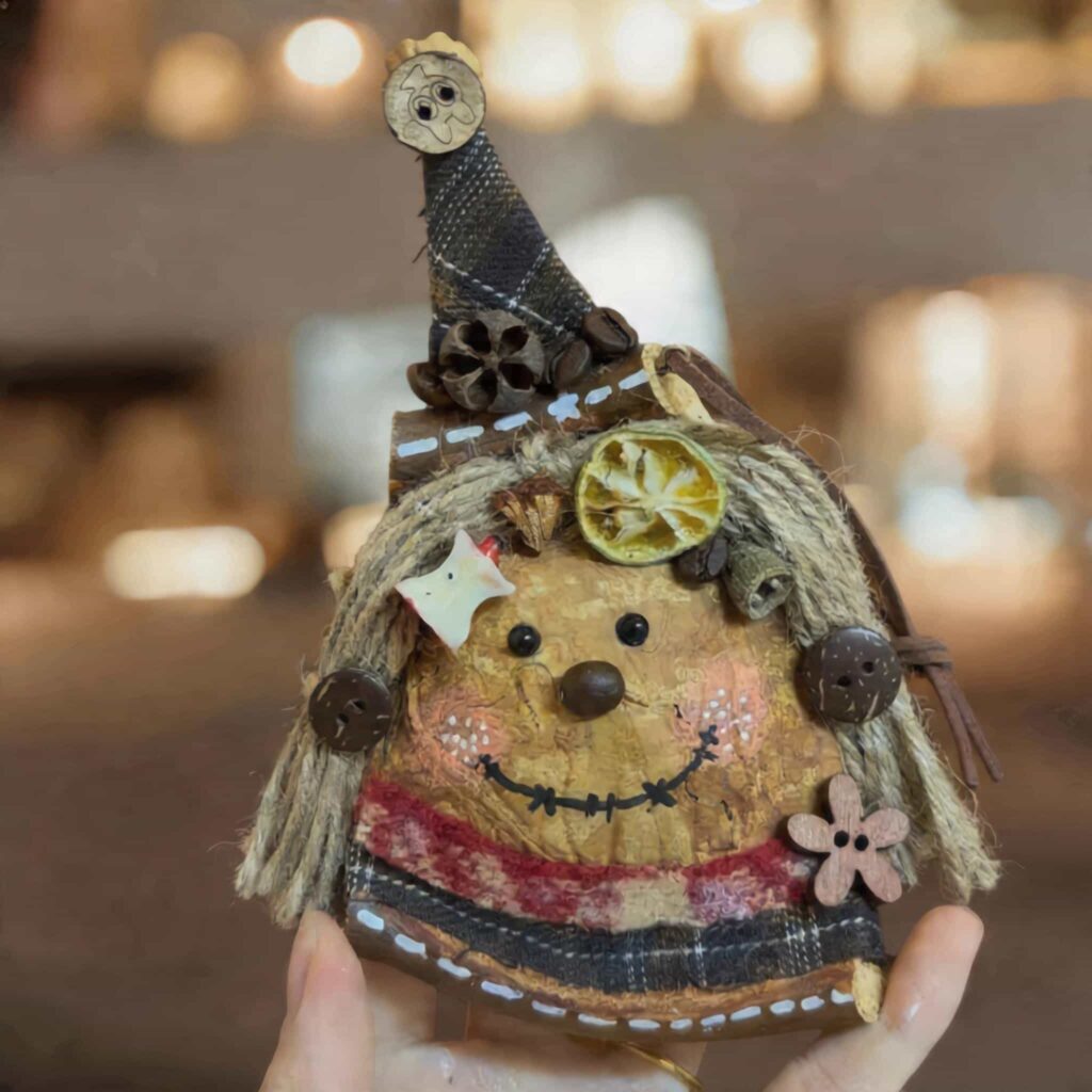 Handmade rustic witch pod doll with stitched smile, rope hair, and pointed hat held in hand