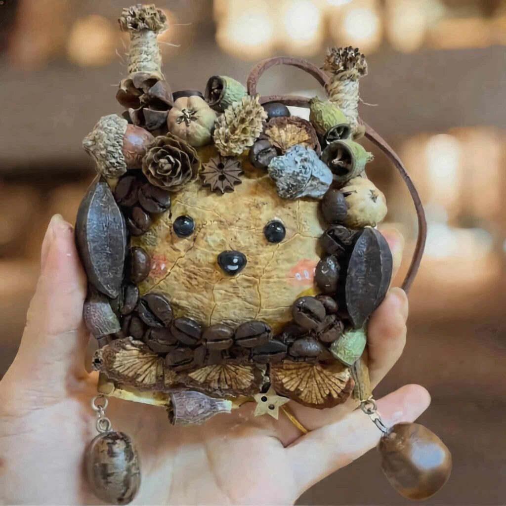 Hand holding finished Coffee Grove Sprite pod doll decorated with coffee beans, acorns, seed pods, and earthy woodland details.