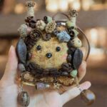 Hand holding finished Coffee Grove Sprite pod doll decorated with coffee beans, acorns, seed pods, and earthy woodland details.