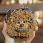 Finished curly cat pod doll shown in hand with soft furry texture, glasses, and playful handmade expression