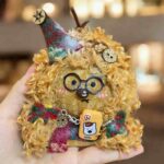 Handmade Fuzzy Glasses Monster Pod Doll held in hand, showing fluffy texture, round glasses, pointed hat, and colorful outfit details
