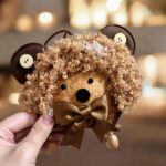 Handmade bear pod doll with curly hair and mocha bow held in hand