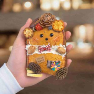 Back side of double-sided pod doll with red bow tie, handmade tag, and pinecone decorations