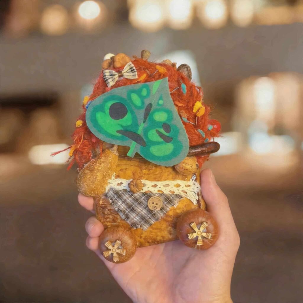 Handheld view of the double-sided pod doll with a magnetic green leaf face attached, showing the interchangeable woodland-inspired face feature.