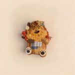 Studio shot of the double-sided handmade pod doll showing the original open-mouth side with glasses, curly beard, plaid patch pocket, and paw-shaped feet.