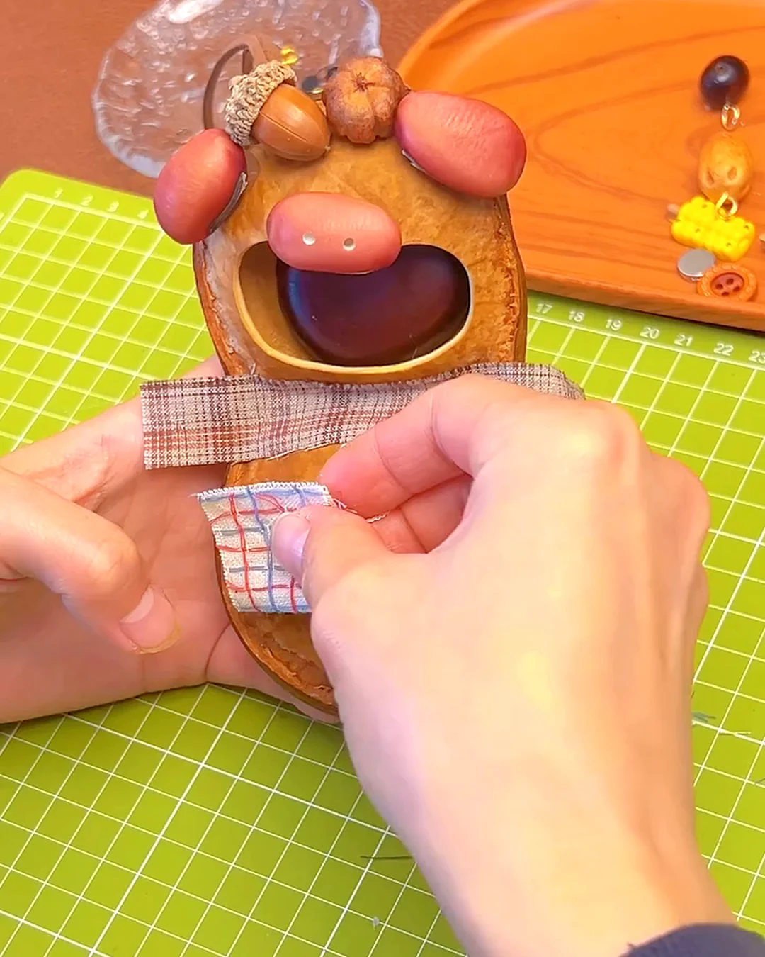 Small fabric details being added by hand to a Poddoll made from a natural seed pod shell.