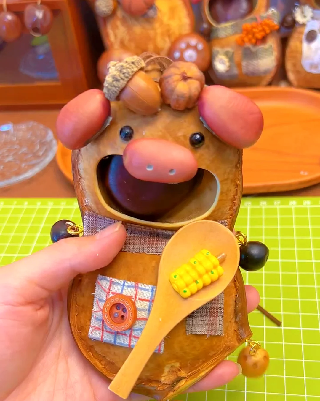 A finished handmade seed pod doll character with fabric details, hanging parts, and a tiny spoon accessory.