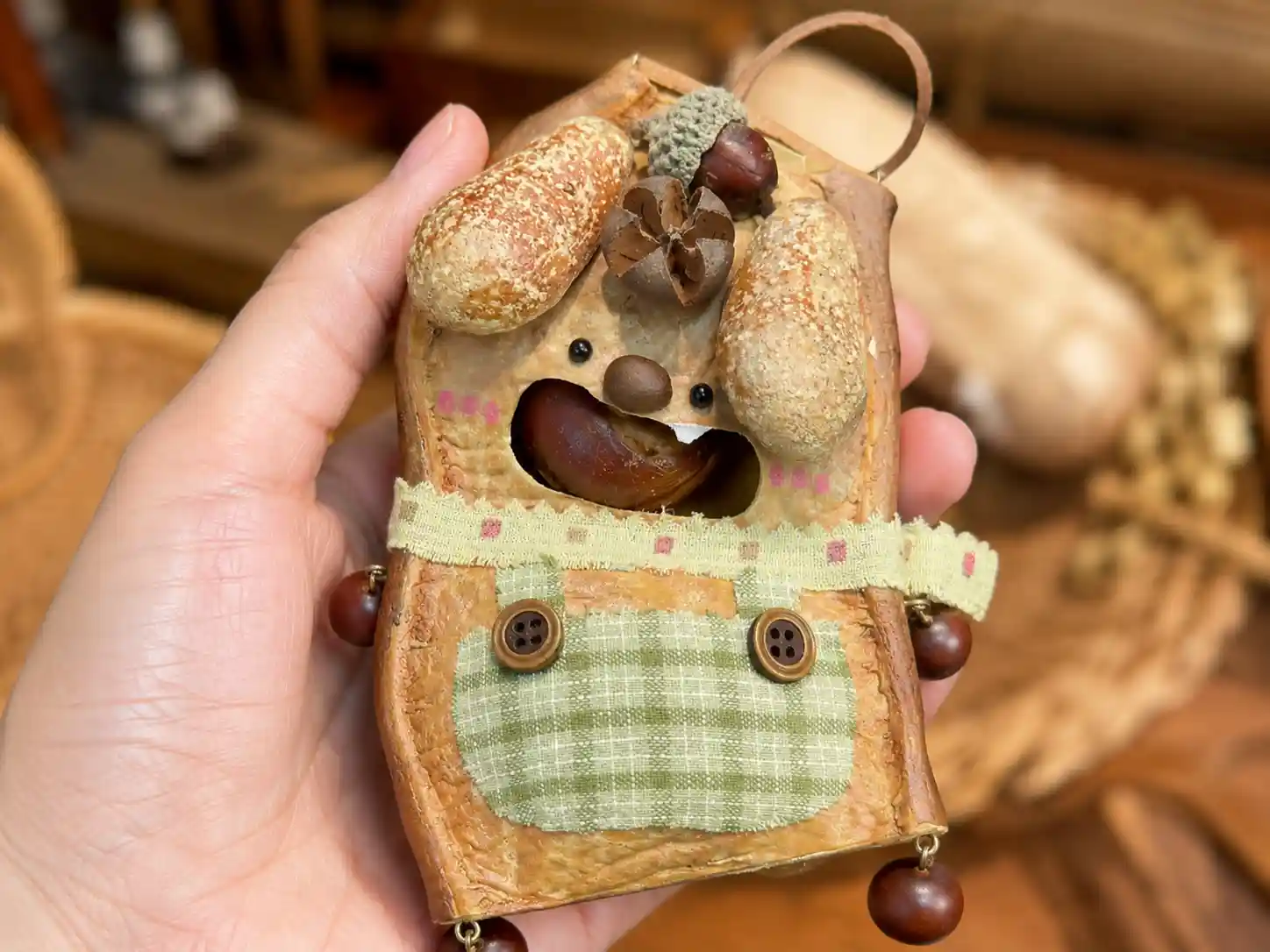 Handheld handmade pod doll showing whole seed pod shell body, added natural seed accessories, fabric apron, and tiny handmade details