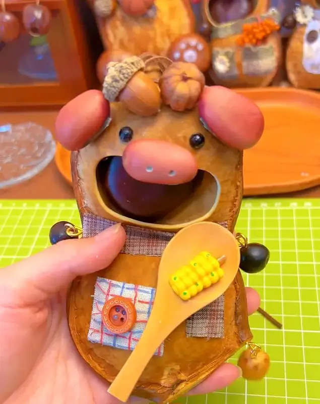 A finished handmade seed pod doll made from a natural seed pod shell with fabric details and tiny accessories.