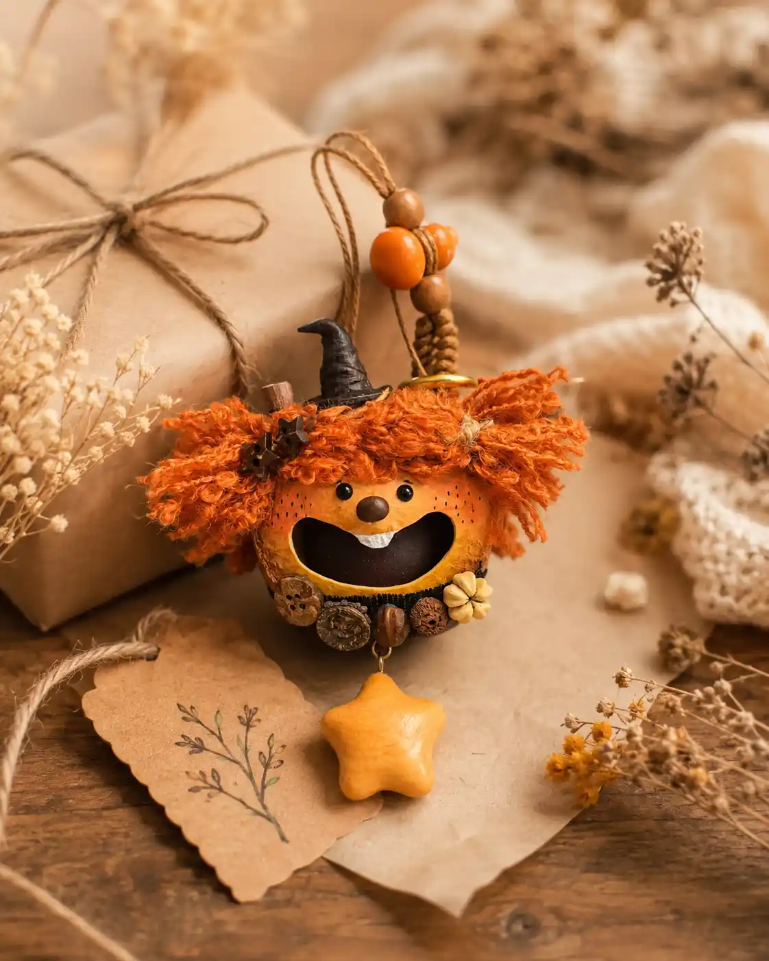Orange-haired handmade pod doll displayed beside a wrapped gift box, dried flowers, and a small gift tag