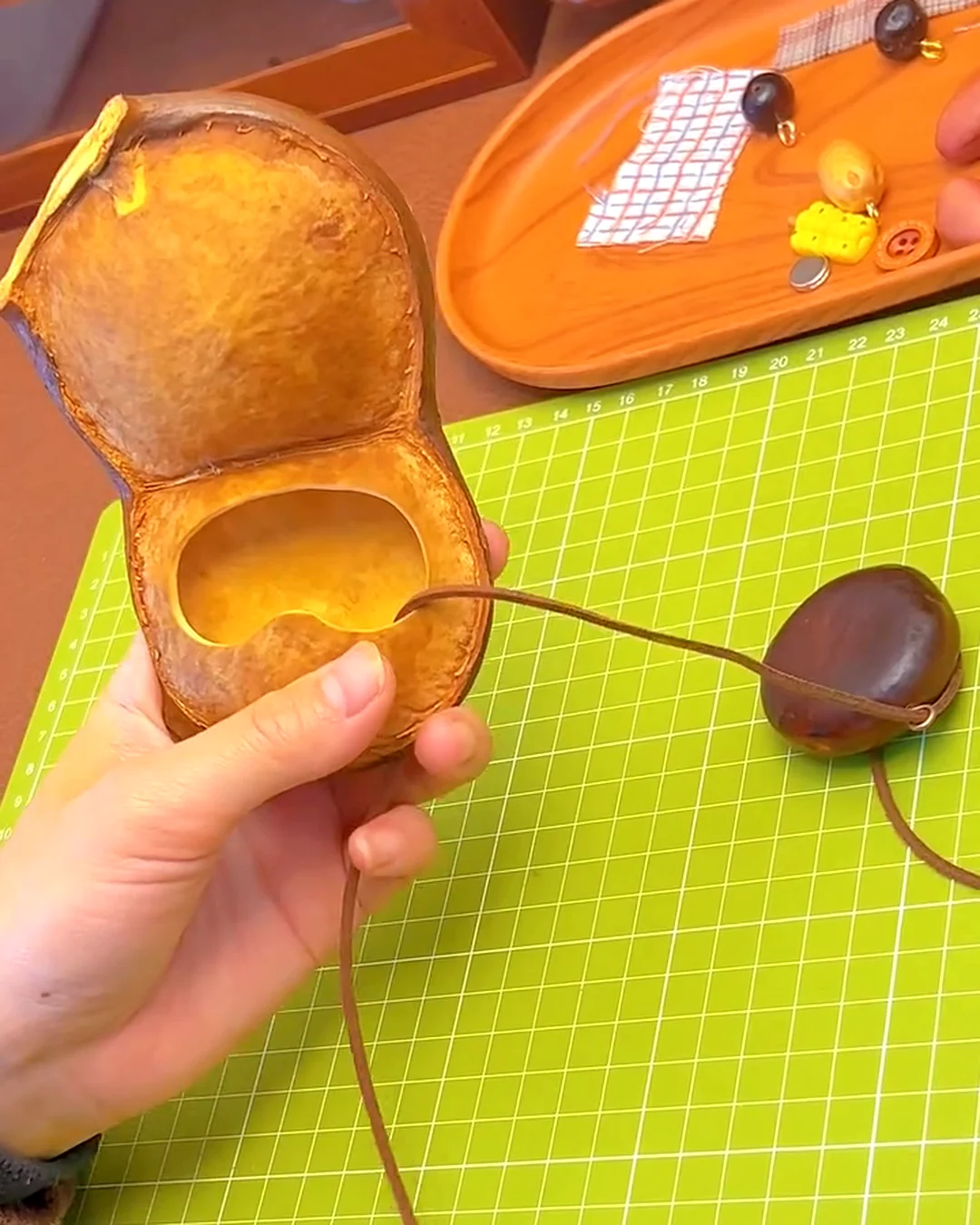 A prepared natural seed pod shell being threaded with cord for a handmade pod doll.