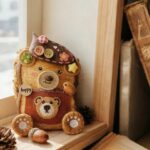 Bear-inspired handmade Poddoll displayed on a wooden window shelf beside books, a pinecone, and a natural acorn