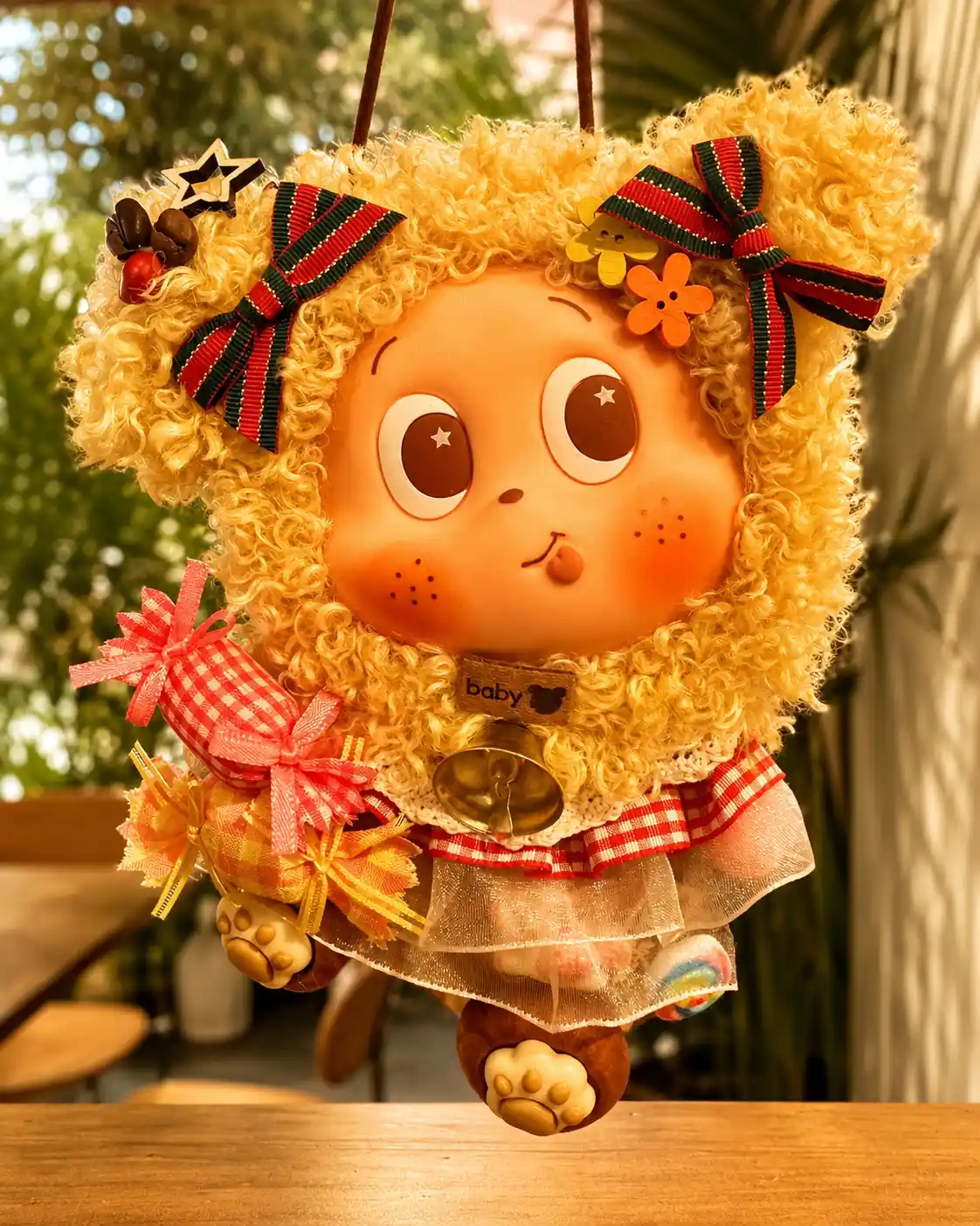 Yellow curly-haired handmade Poddoll hanging by a window with striped bows, fabric gifts, a bell, and paw-shaped feet