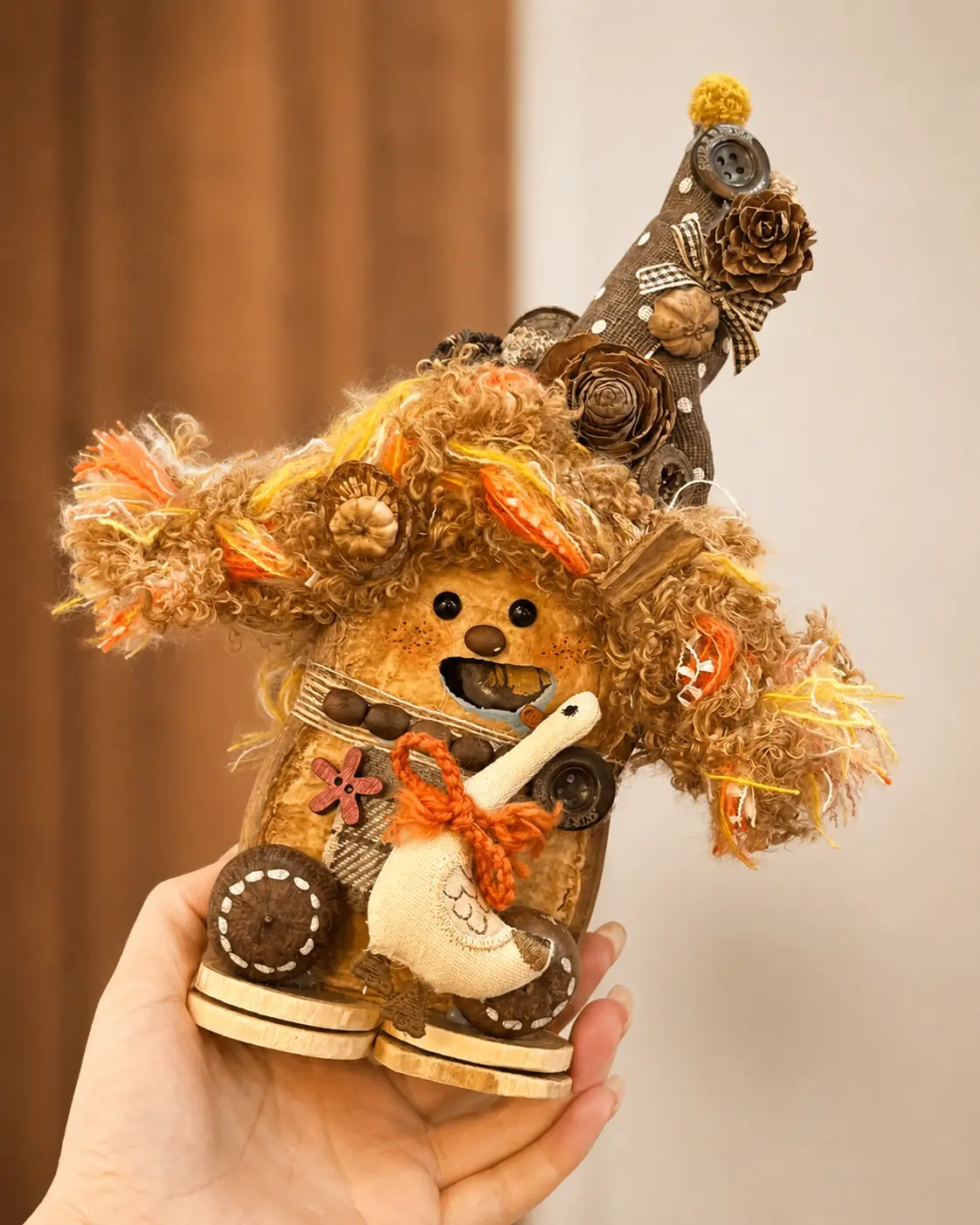 Hand holding a curly-haired animal-inspired Poddoll with a tall decorated hat, floppy ears, natural decorations, and a small fabric goose