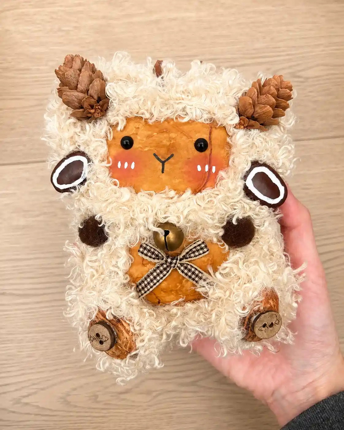 Handmade sheep-like Poddoll with white curly fleece, pinecone horns, a bell, and a plaid bow