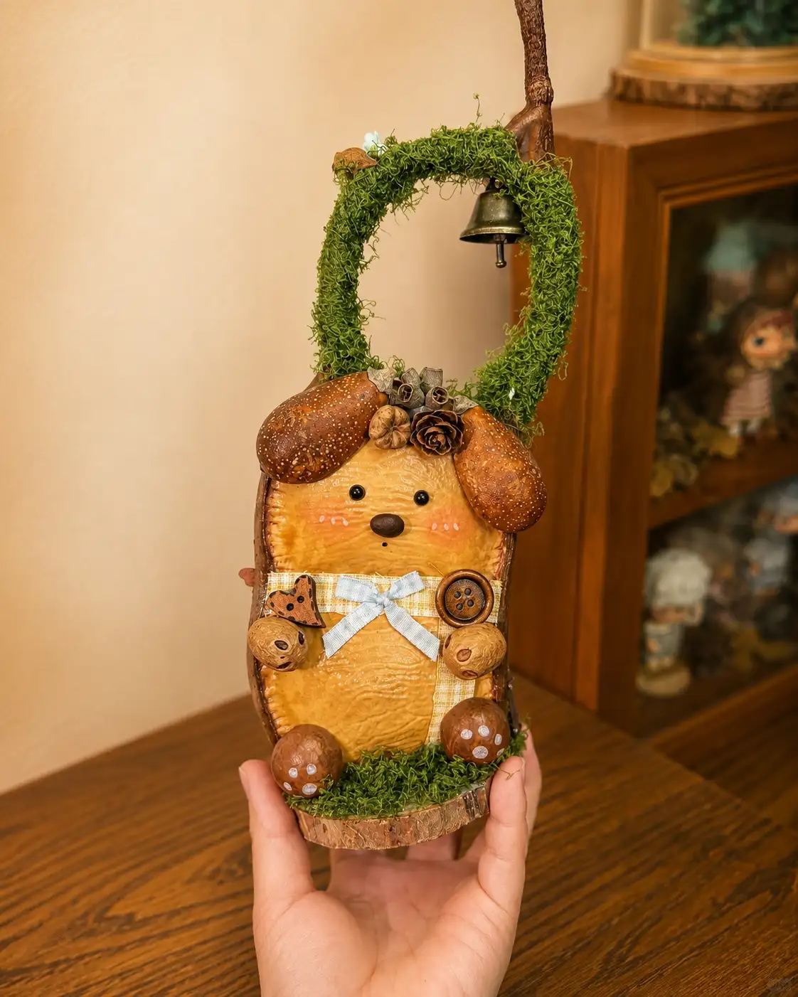 Back of a double-sided Poddoll showing a handmade dog-like character with natural ears, a blue bow, buttons, and a moss-covered handle