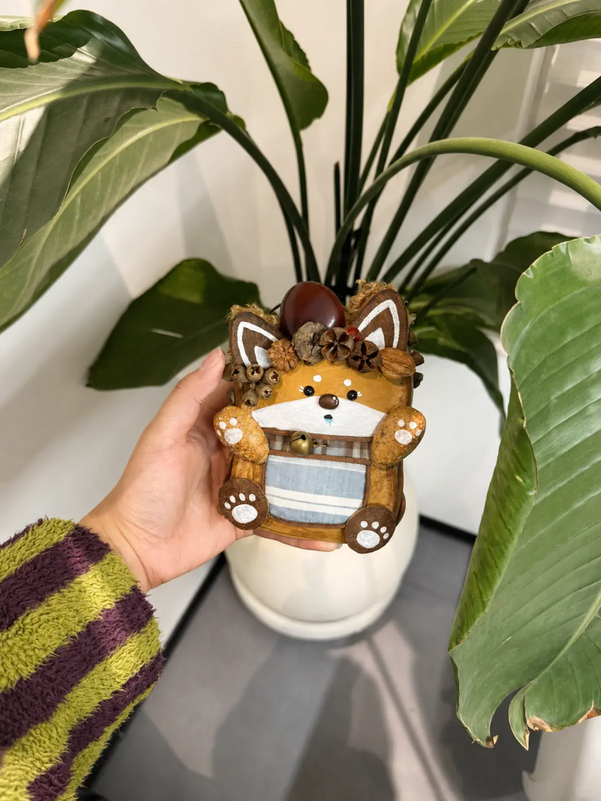 Handmade fox Poddoll held beside a large indoor houseplant