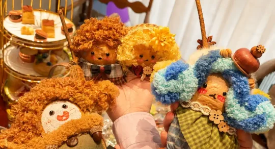 Several hands holding four different handmade Poddoll characters at an indoor celebration