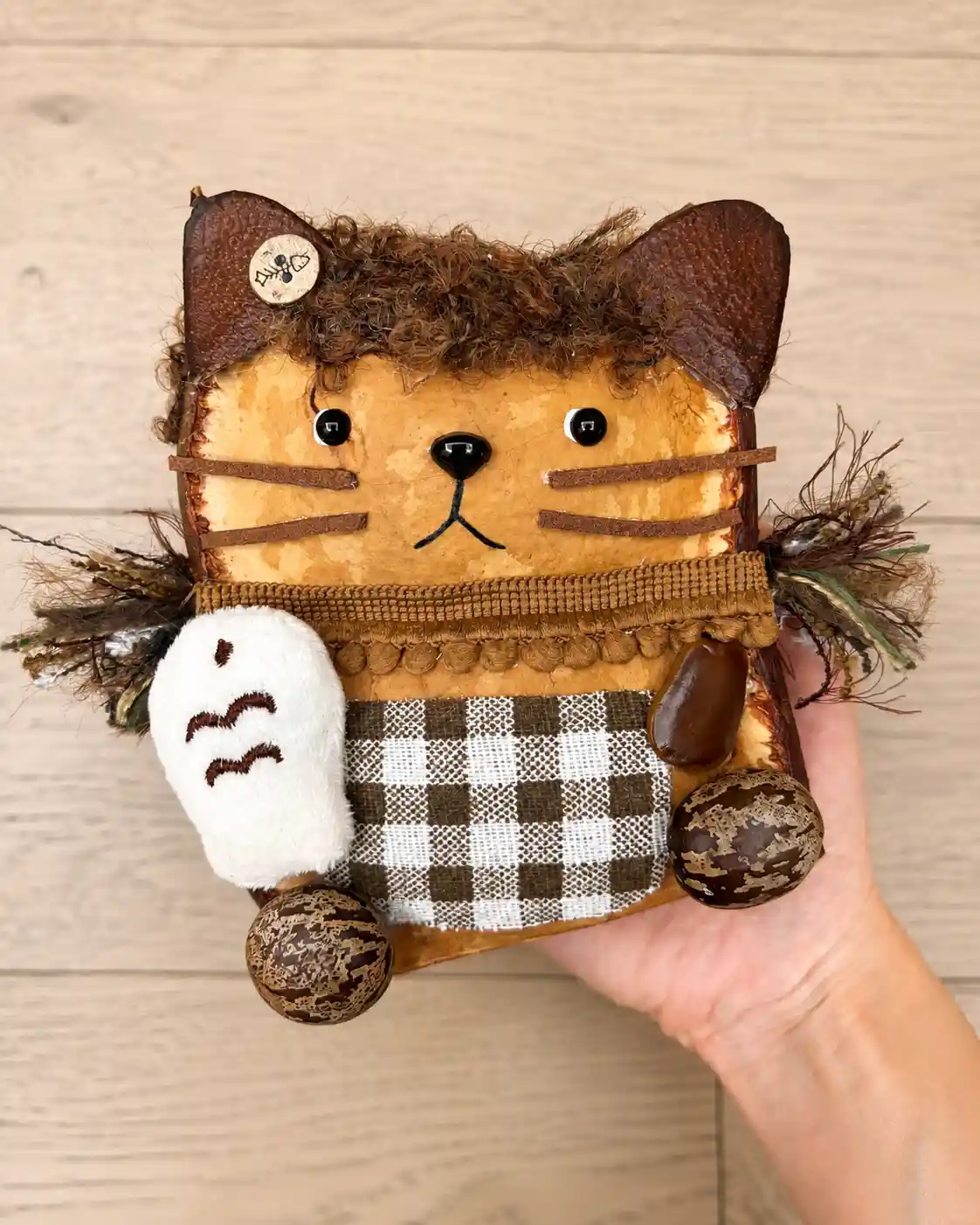 Handmade cat-like Poddoll with dark ears, whiskers, plaid clothing, and natural seed pod paws