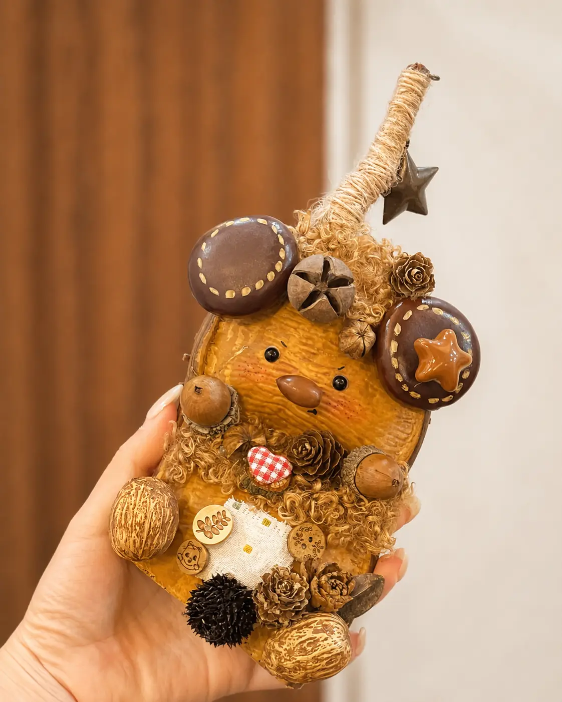 Hand holding a round-eared animal-inspired Poddoll with a tall wrapped hat, hanging star, acorns, pinecones, buttons, and curly fiber details