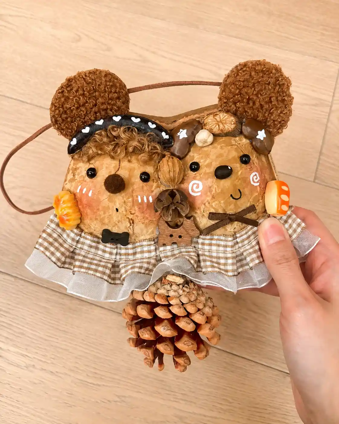 Handmade hanging Poddoll with two animal-inspired faces, plaid clothing, curly ears, and a pinecone pendant
