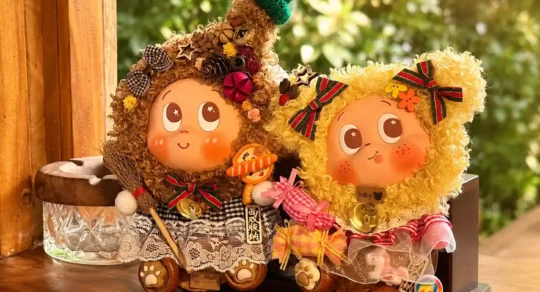 Two finished handmade Poddolls with brown and yellow curly hair, bows, lace clothing, bells, and small character accessories