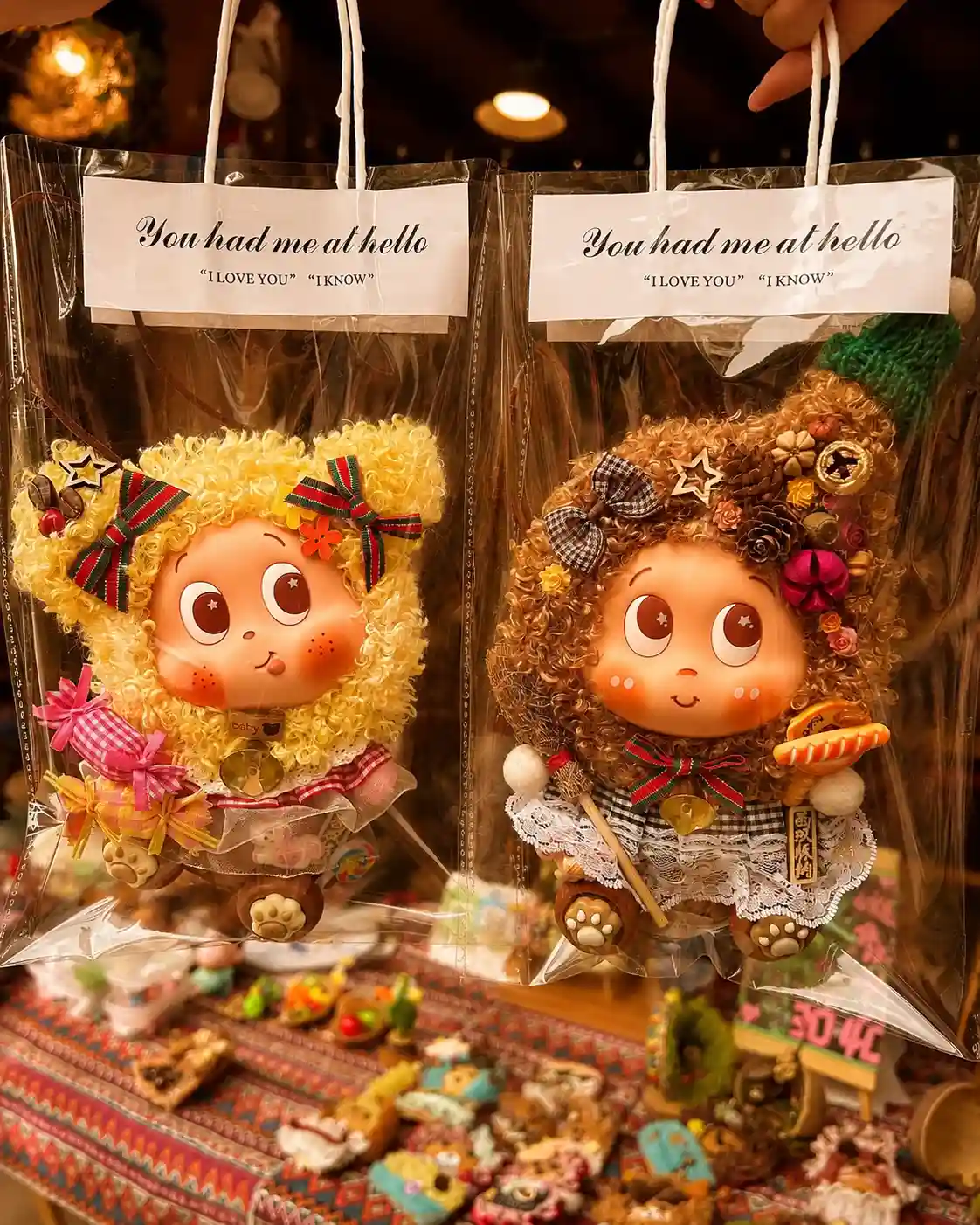 Two finished handmade Poddolls packaged separately in clear handled bags above a craft display table